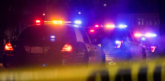 Dad Drives Family to Safety—With Bullet in His Head! Police cars with flashing lights at a nighttime scene behind crime scene tape