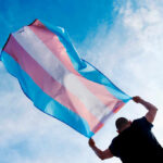 Person holding a transgender pride flag against a blue sky