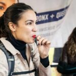 AOC’s SHOCKING 2028 Rejection—What’s She Planning? A woman enjoying a snack at an outdoor event with a smiling companion in the background