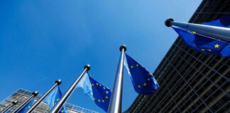 Europe Quietly Rewrites Rights for More Deportations European Union flags flying in front of a modern building against a clear blue sky