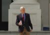man in blazer holding a soda can on building steps