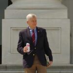 man in blazer holding a soda can on building steps