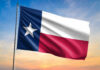 Texas state flag waving against a sunset sky