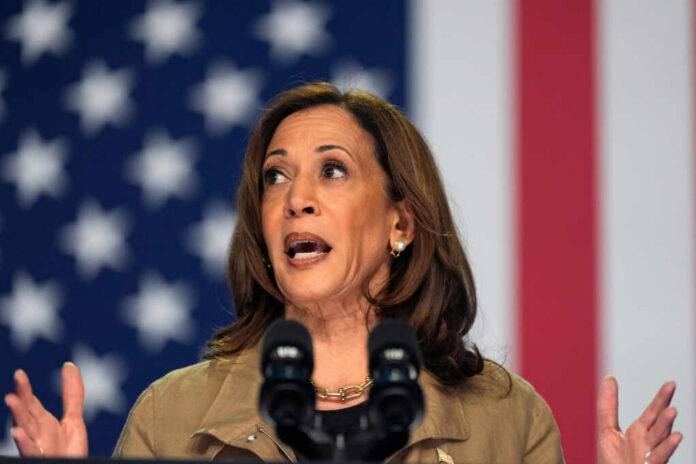 A woman speaking passionately at a podium with microphones against an American flag backdrop