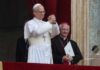 A religious leader in white robes gestures during a public address