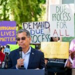 Speaker addressing a crowd at an immigration rights rally with protest signs in the background