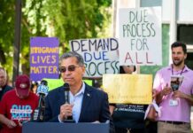 Speaker addressing a crowd at an immigration rights rally with protest signs in the background
