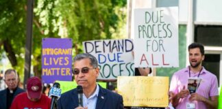 Speaker addressing a crowd at an immigration rights rally with protest signs in the background