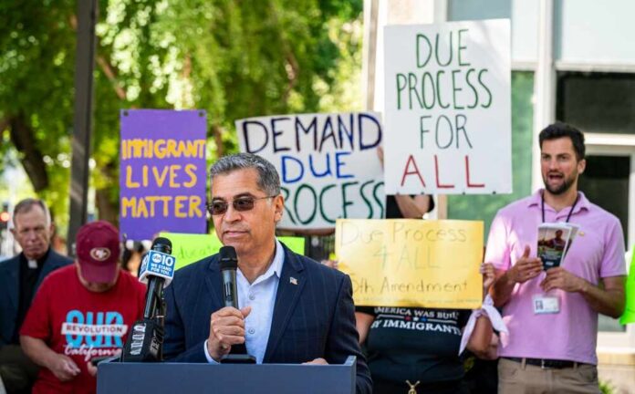 Speaker addressing a crowd at an immigration rights rally with protest signs in the background