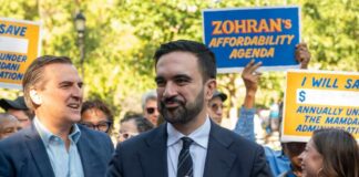 A politician speaking at a rally with supporters holding signs