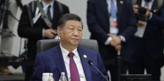 A seated leader at a conference table with a nameplate indicating the People's Republic of China