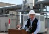 Man in a hard hat speaking at a podium in an industrial setting