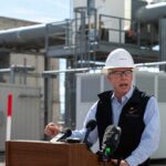 Man in a hard hat speaking at a podium in an industrial setting