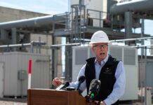 Man in a hard hat speaking at a podium in an industrial setting