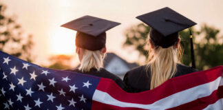 Two graduates wearing caps holding an American flag during sunset