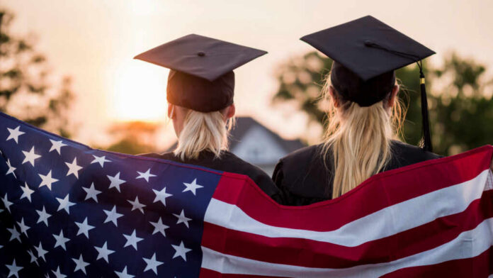 Two graduates wearing caps holding an American flag during sunset