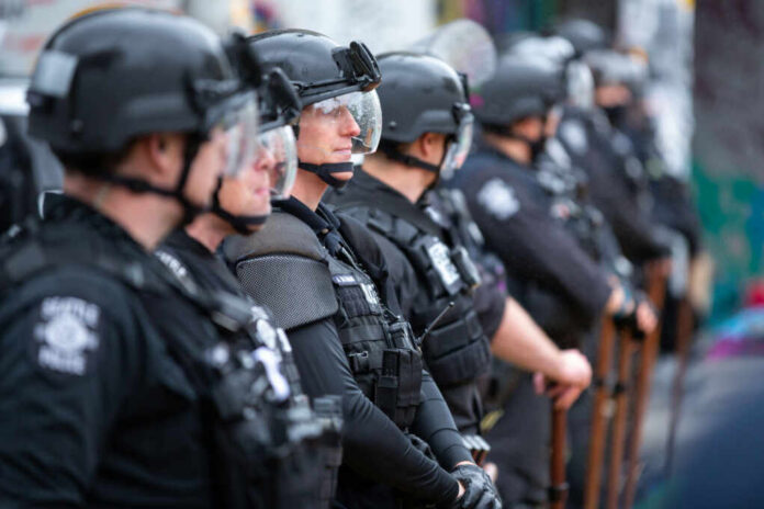 shutterstock1767784172jpg Line of riot police in tactical gear standing ready for crowd control