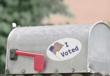 A metal mailbox with an I Voted sticker and an American flag design
