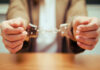 Fraud-Fluencers Busted Flaunting Stolen Cash Close-up of hands holding handcuffs in a serious context