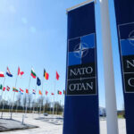 NATO flags displayed in front of the NATO headquarters under a clear blue sky