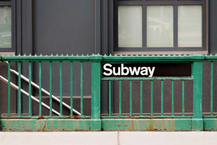 Subway entrance with a green railing and a sign reading Subway