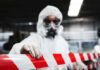 Worker in protective gear holding a red and white barrier tape in an industrial environment