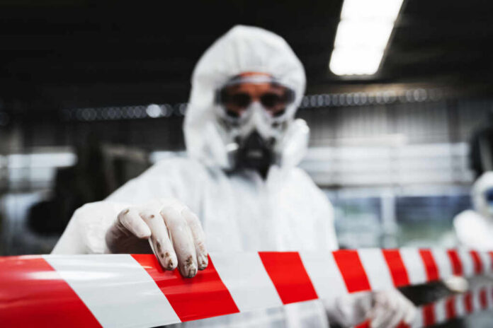shutterstock2455268667jpg Worker in protective gear holding a red and white barrier tape in an industrial environment