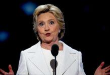 A woman in a white suit speaking at a podium during a conference