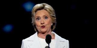 A woman in a white suit speaking at a podium during a conference