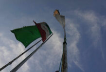 Iranian Caught Smuggling U.S. Military Tech to Iran Through China Two flags on a flagpole against a blue sky with clouds