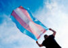 FTC Goes Nuclear on Trans Guidelines Person holding a transgender pride flag against a blue sky
