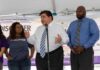 man speaking at a podium with three people standing beside him