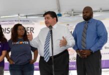 Trump Dares Pritzker: Call For Help man speaking at a podium with three people standing beside him