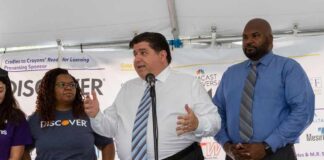 man speaking at a podium with three people standing beside him