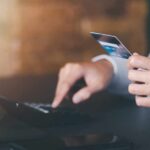 Person holding a credit card while using a calculator at a desk