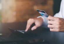 Person holding a credit card while using a calculator at a desk