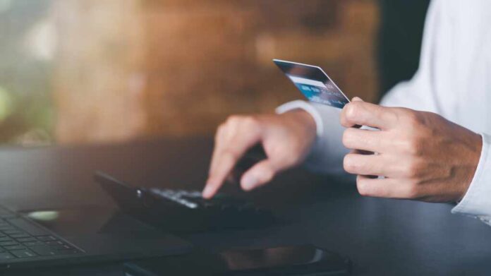 Person holding a credit card while using a calculator at a desk