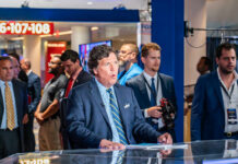 News anchor speaking in a television studio with crew members in the background