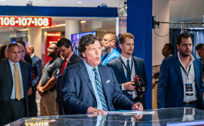 News anchor speaking in a television studio with crew members in the background