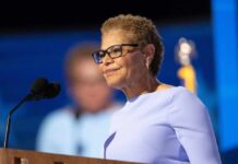 A woman in a light blue dress speaking at a podium with a microphone