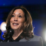 DOJ Whiplash Coming? Harris Teases Crackdown A female politician speaking at a podium with microphones in front of her