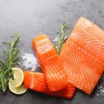Fresh salmon fillets with lemon and herbs on a dark surface