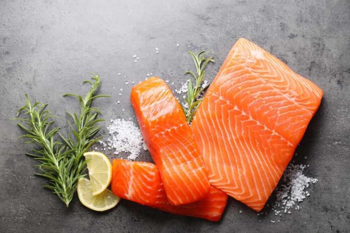 Fresh salmon fillets with lemon and herbs on a dark surface