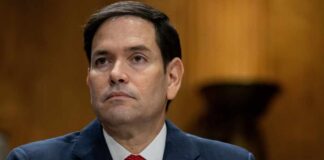 A government official sitting at a hearing with a serious expression