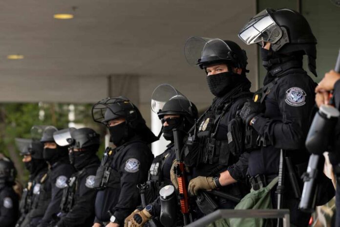 Los,Angeles,,California,,Usa,-,June,10,,2025:,U.s.,Customs A police officer in a tactical vest stands near a barbed wire fence with an American flag in the background