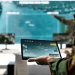 Soldier holding a tablet in a command center with digital maps on screens