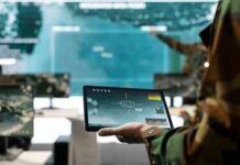 Soldier holding a tablet in a command center with digital maps on screens