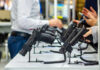 Court Loophole Lets Guns Get Seized? Display of handguns at a firearms exhibition with attendees interacting
