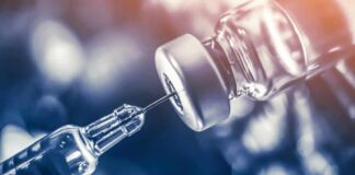 syringe needle drawing liquid from a vaccine vial