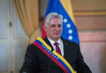 Man in suit wearing a tricolor sash seated at a podium
